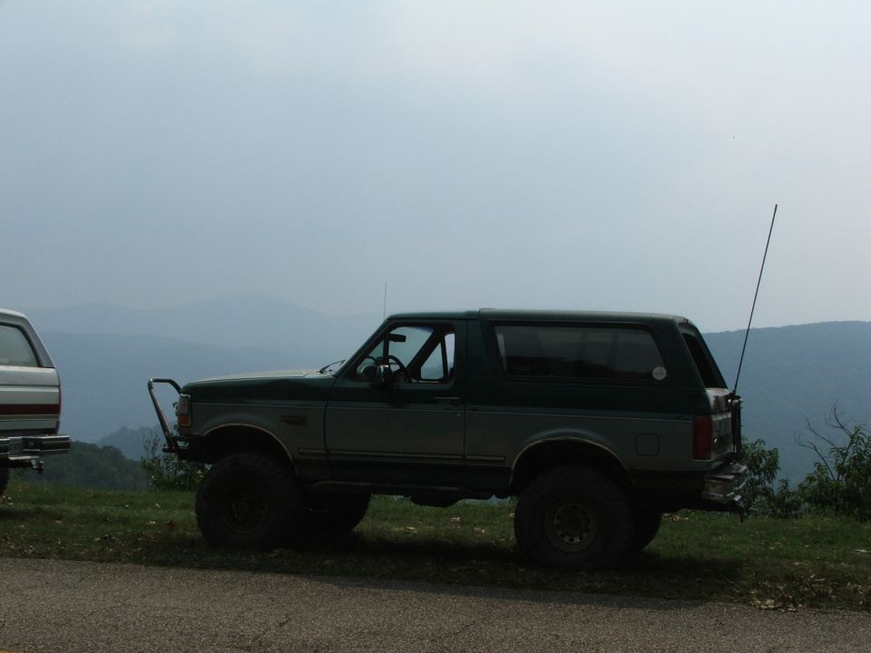 Two-tone green and gray Ford Bronco parked on a grassy overlook with mountains in the background