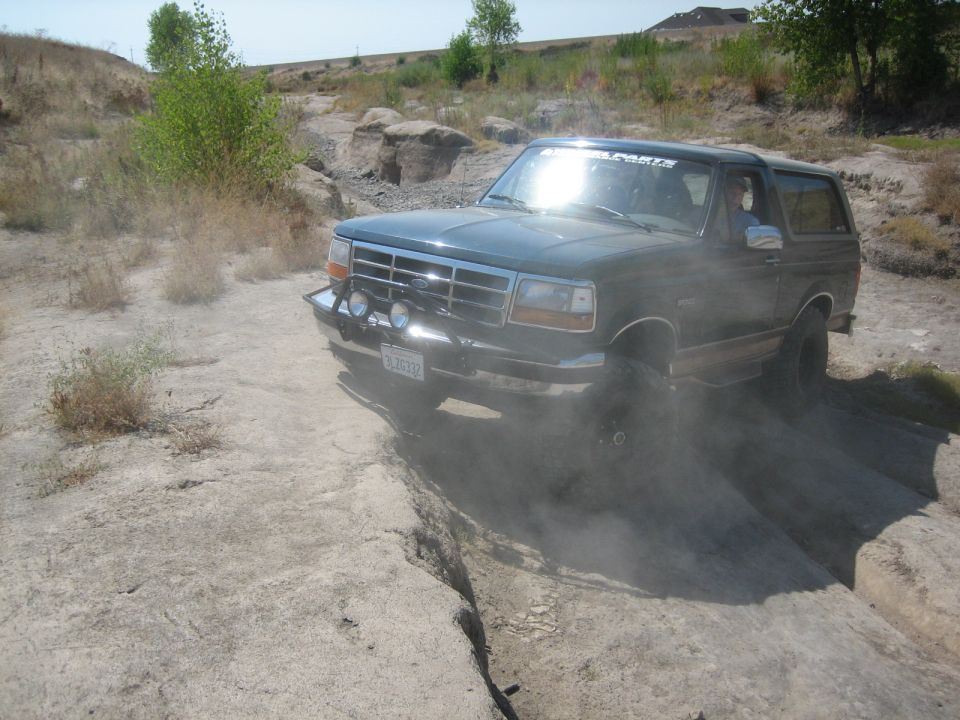 1995 Ford Bronco 3q-front view off-road. Dark green SUV navigating rocky terrain