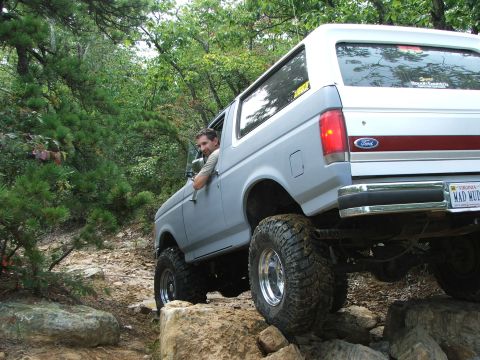 1996 Ford Bronco - A 1996 Ford Bronco navigates a rocky off-road course surrounded by trees.