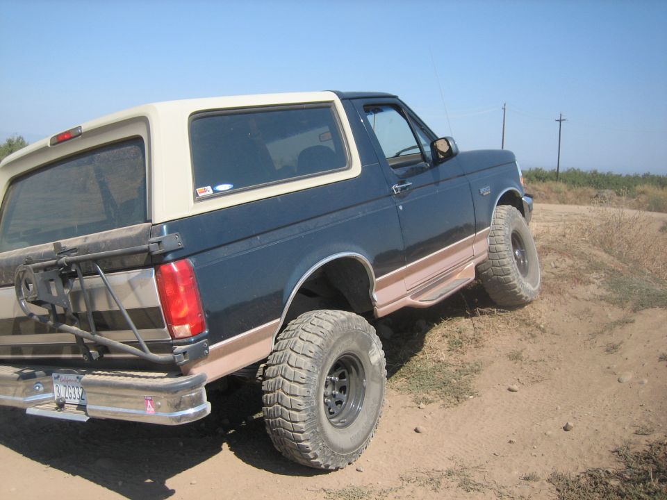 Dark blue and tan Ford Bronco with off-road tires on a dirt hill