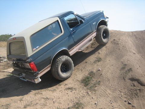 1995 Ford Bronco - A 1995 Ford Bronco navigates an off-road trail, ascending a steep dirt incline.