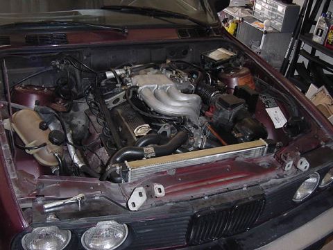 1984 BMW 3 Series - The engine bay of a maroon 1984 BMW 3 Series shows its V6 engine and associated components.