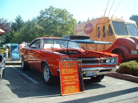 2000 Ford Crown Victoria - A red 1969 Dodge Charger is displayed with its hood open, parked beside a vintage Dari-Gold milk truck.