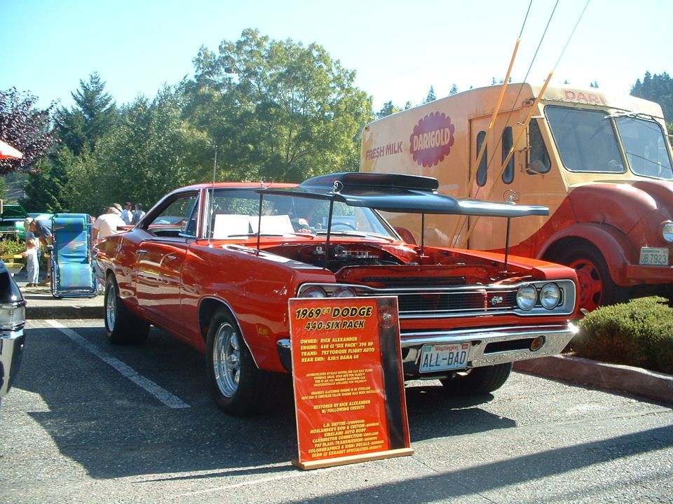 Red 1969 Dodge Charger with hood open, parked next to a vintage milk truck