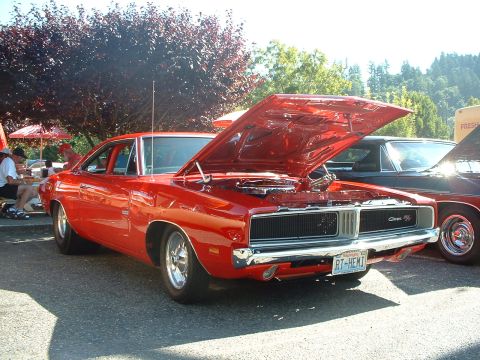 2000 Ford Crown Victoria - A bright red 1969 Dodge Charger is displayed with its hood open, parked alongside another vehicle.
