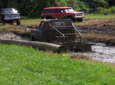 1979 Ford Bronco - Several vehicles navigate a muddy off-road course with trees and grass surrounding the area.