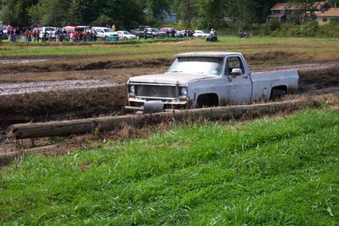 1979 Ford Bronco - A white pickup truck is stuck in a muddy track with spectators in the background.