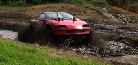 1979 Ford Bronco - Modified red car with snorkel exhaust pipes navigates a muddy obstacle course.