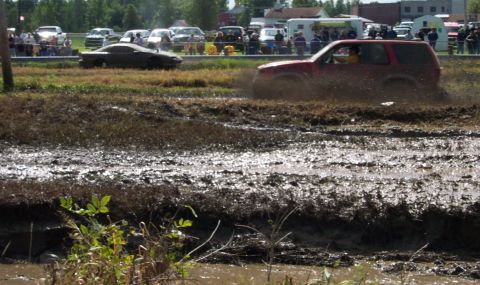 1979 Ford Bronco - A red SUV navigates a muddy obstacle course, kicking up water and dirt.