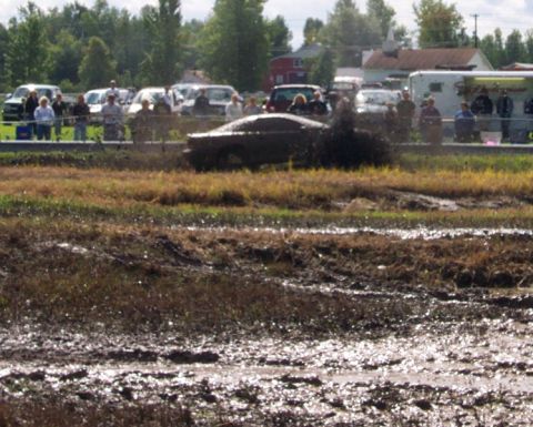1979 Ford Bronco - A vehicle is stuck in a mud pit during an event, with onlookers in the background.