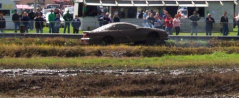 1979 Ford Bronco - A car is stuck in the mud during an event, with a crowd of onlookers observing the scene.