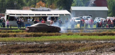 1979 Ford Bronco - A car is stuck in the mud, creating smoke, while onlookers observe the scene.