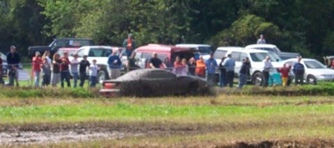 1979 Ford Bronco - A car is stuck in a muddy field with onlookers gathered nearby.