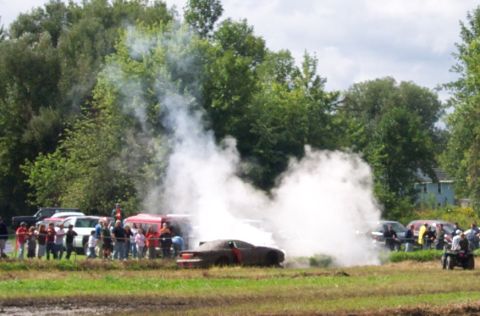 1979 Ford Bronco - A car is stuck in the mud, emitting smoke, while a crowd watches the event.
