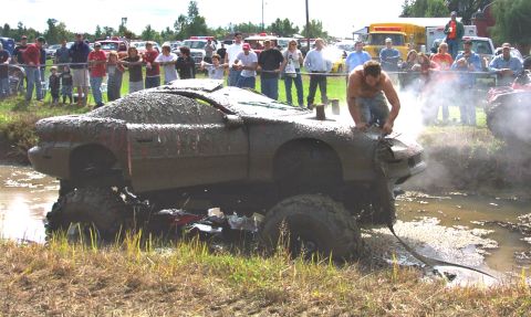 1979 Ford Bronco - A heavily mud-caked car is stuck in a mire, with onlookers gathered around.