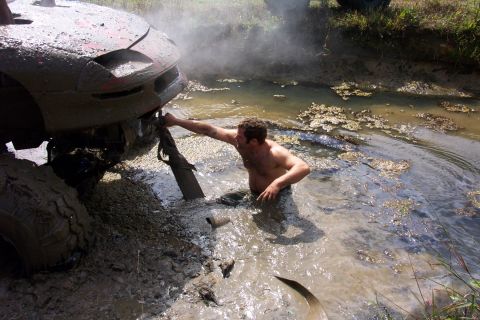1979 Ford Bronco - A person attempts to free a mud-covered car stuck in a body of water.