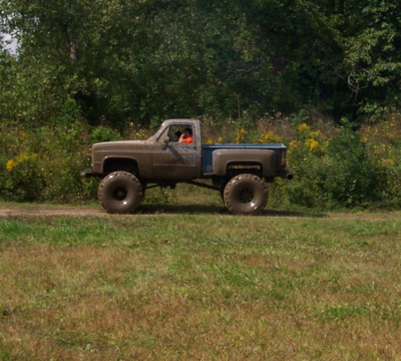 Brown and blue lifted pickup truck with large tires driving on a dirt road