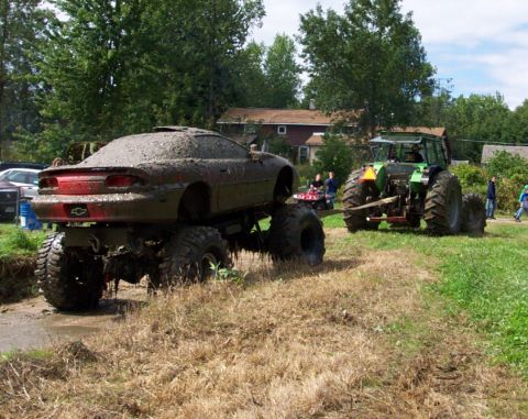 1979 Ford Bronco - A mud-covered car with monster truck wheels is being towed by a tractor in a muddy field.