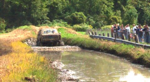 1979 Ford Bronco - Off-road vehicle navigates a muddy water crossing with onlookers watching.