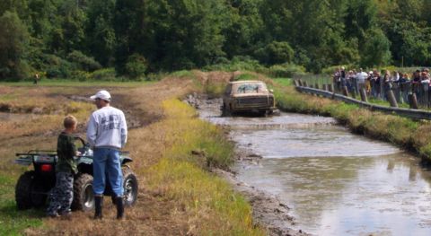 1979 Ford Bronco - A truck navigates a muddy track while onlookers observe from the side.