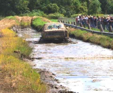 1979 Ford Bronco - A yellow 1979 Ford Bronco navigates a muddy track with spectators watching from the side.
