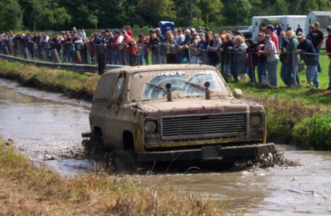 1979 Ford Bronco - This SUV is covered in mud as it navigates a challenging mud bog, watched by a crowd.