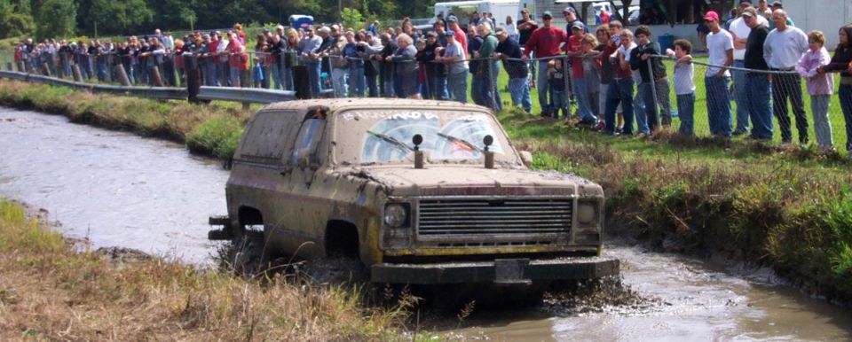 Muddy SUV navigating a mud pit with spectators watching