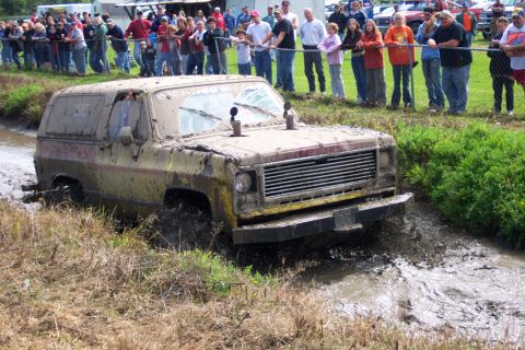 1979 Ford Bronco - This SUV is deep in the mud during an off-road event, with a crowd observing the action.