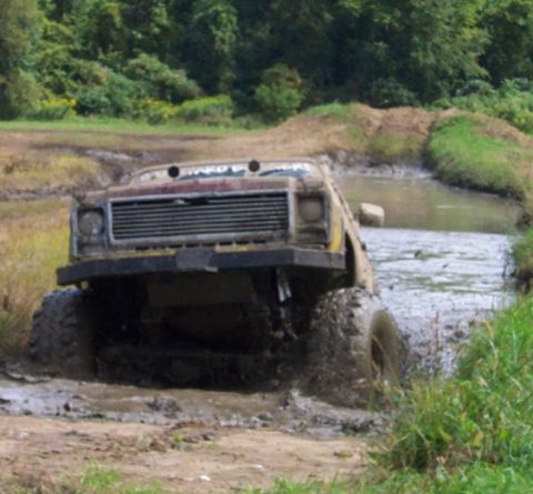 1979 Ford Bronco - Off-road truck navigates a challenging muddy water crossing with significant splash.