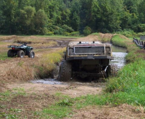 1979 Ford Bronco - A heavily modified truck navigates a muddy off-road course with an ATV in the background.