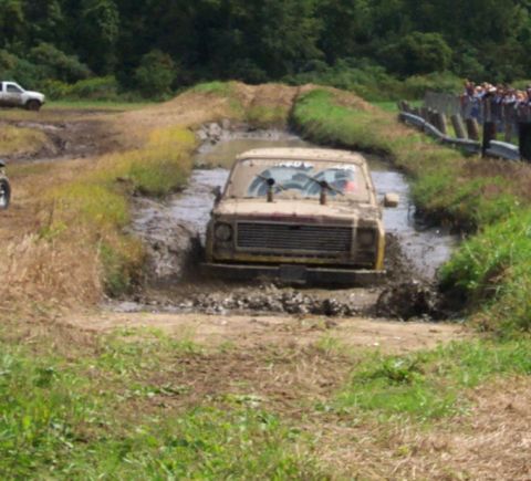 1979 Ford Bronco - A pickup truck navigates a muddy obstacle course with spectators watching from the side.