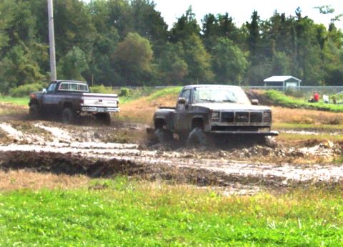 1979 Ford Bronco - Two pickup trucks navigate a muddy track, kicking up dirt and water.