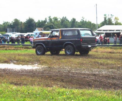 1979 Ford Bronco - Ford Bronco navigates a muddy track with onlookers present.