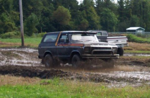 1979 Ford Bronco - A dark blue 1978 Ford Bronco navigates a muddy track, with another truck visible in the background.