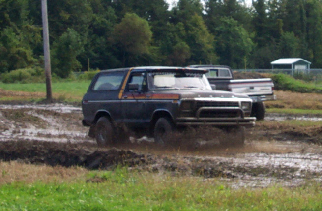 Dark blue 1978 Ford Bronco with orange stripe driving through mud