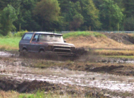 1979 Ford Bronco - Ford Bronco navigating a muddy off-road course, tires deep in the mire.