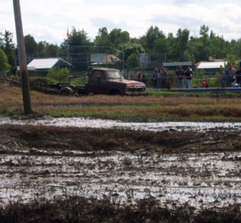 1979 Ford Bronco - A red pickup truck is stuck in a muddy field with spectators in the background.