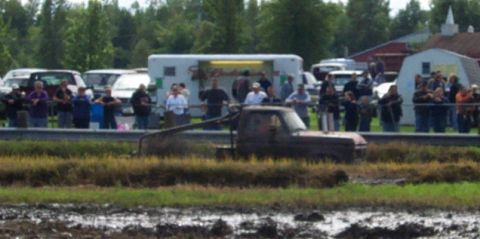 1979 Ford Bronco - A pickup truck navigates a muddy course as onlookers observe the event.