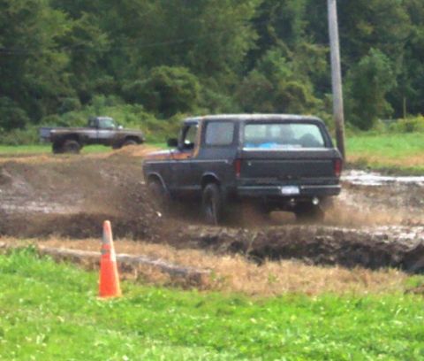 1979 Ford Bronco - A dark-colored Ford Bronco navigates a muddy track, with another truck visible in the distance.
