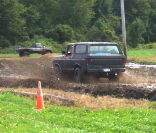 Dark Ford Bronco driving through mud, another truck in background