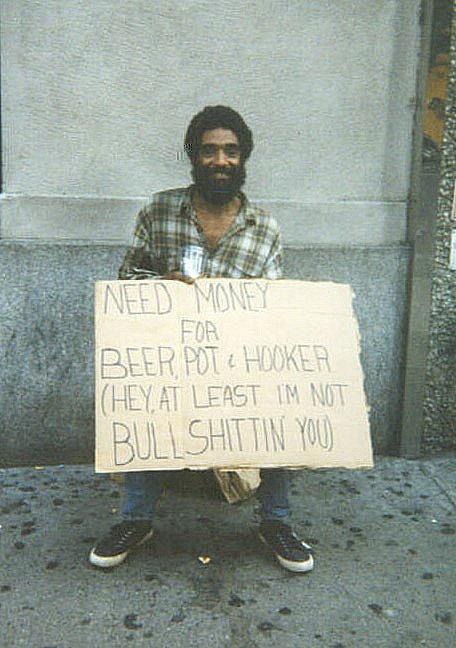 1999 Ford Crown Victoria - A man sits on a sidewalk holding a sign that humorously states his needs, including money for beer, pot, and a hooker.