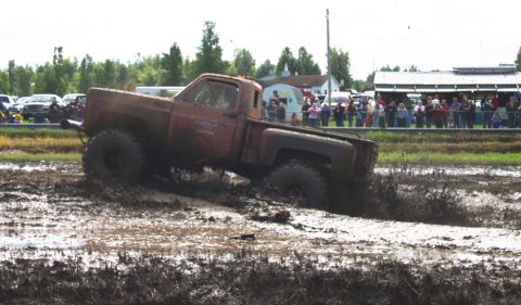 1979 Ford Bronco - Pickup truck navigates a mud bog with spectators watching from the sidelines.