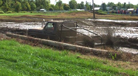 1979 Ford Bronco - Pickup truck navigates a muddy obstacle course, kicking up mud.