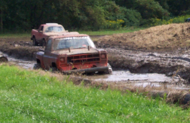 Two red trucks stuck in a mud pit with grassy banks