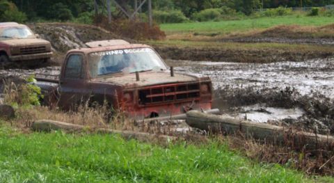 1979 Ford Bronco - Trucks are navigating a muddy track, with one vehicle partially submerged in the mire.