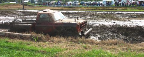 1979 Ford Bronco - A red pickup truck is stuck deep in a mud pit during an event.