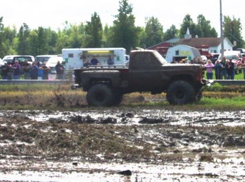 1979 Ford Bronco - A heavily muddied pickup truck navigates a muddy track with spectators in the background.