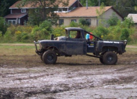 1979 Ford Bronco - Modified black pickup truck with off-road tires and roll cage drives through muddy terrain.