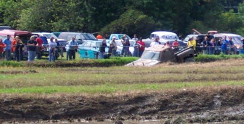 1979 Ford Bronco - Spectators watch as a truck becomes stuck in a mud pit during an event.