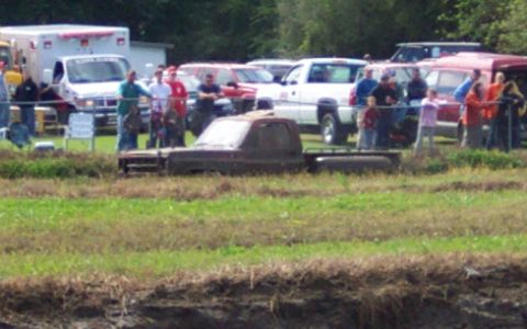 1979 Ford Bronco - A group of people watch as a truck sits in a muddy field.
